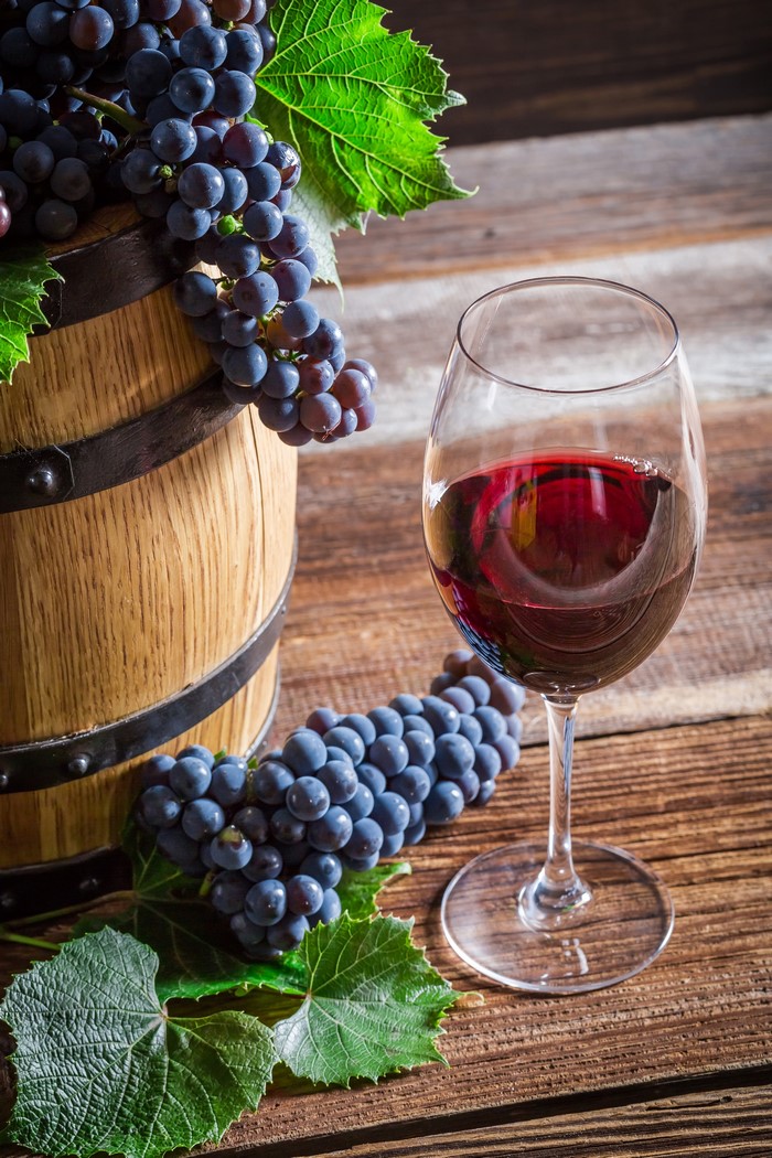 Red wine in a glass with grapes and a barrel
