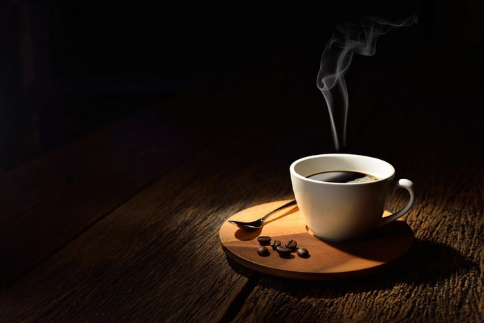 Cup of coffee with steam and coffee beans on wood