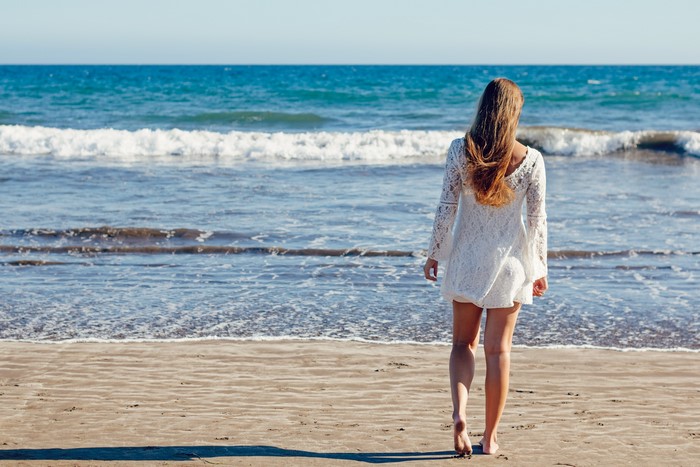 Woman in white dress walking on beach towards the sea
