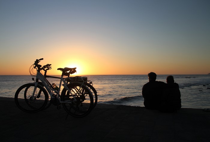 Two people and bicycles watching the sunset over the sea