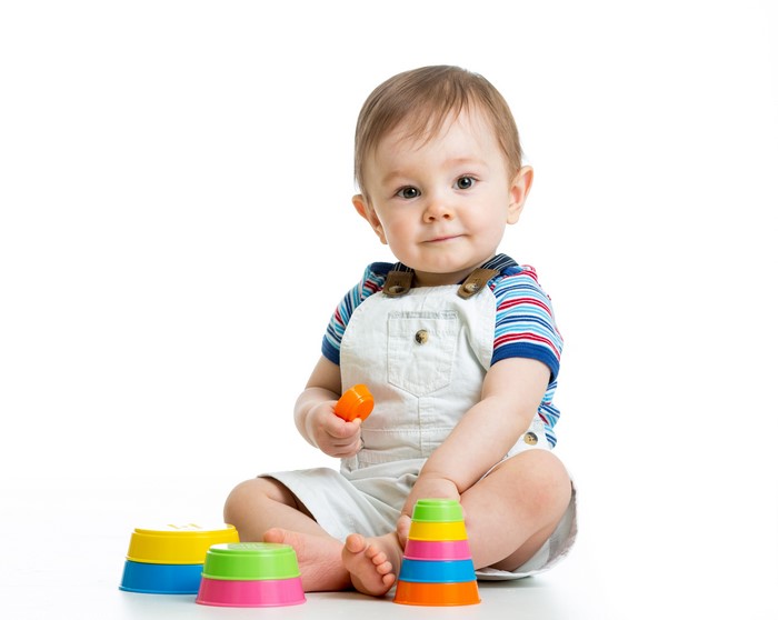 Baby boy playing with stacking toys on white background