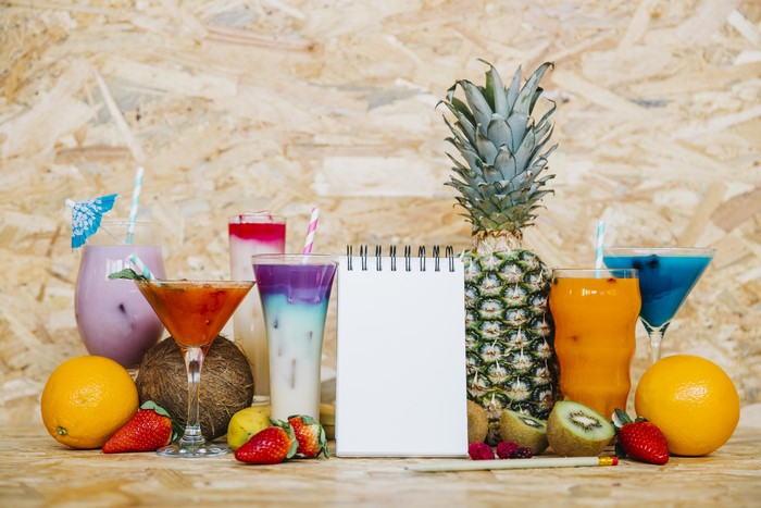 Assortment of tropical fruits and colorful cocktails with a notepad