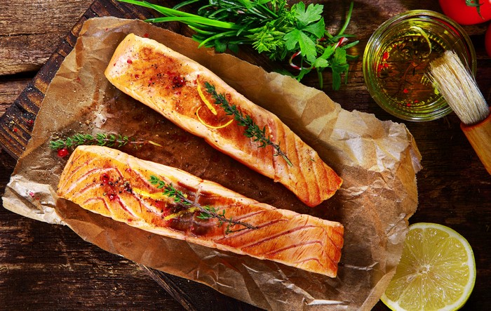 Two salmon fillets with herbs and lemon on parchment paper