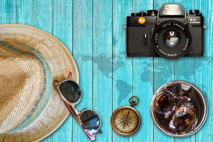Travel essentials: Hat, sunglasses, camera, compass, and drink on wood