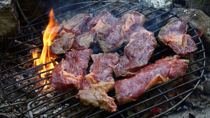 Raw meat cooking on a grill over a bonfire