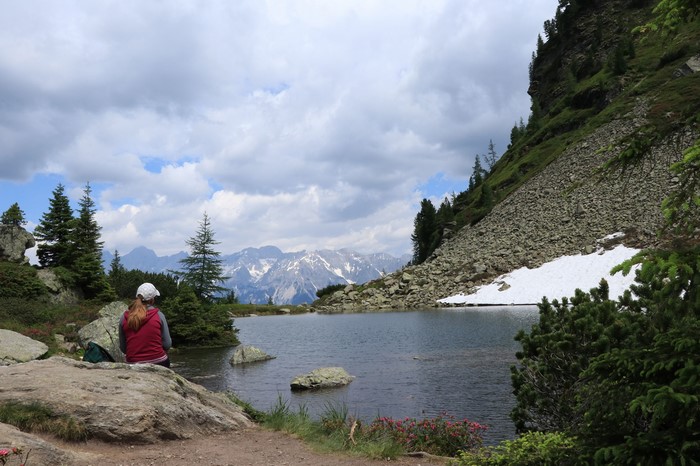 Girl sitting by a mountain lake with snow-capped peaks