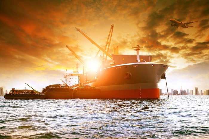 Cargo ships and airplane at sunset