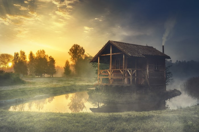 Wooden house by a foggy lake at sunrise