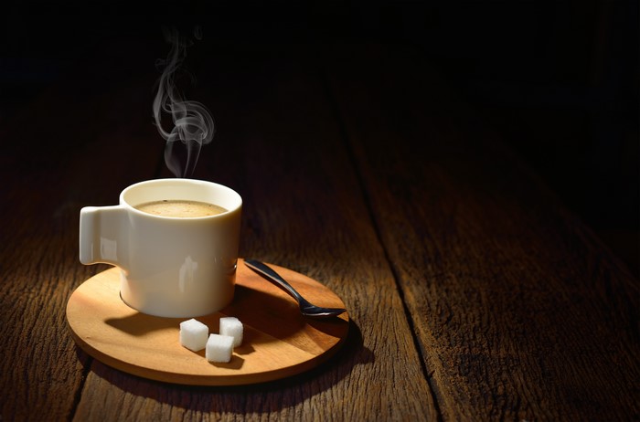 Coffee cup with steam, sugar cubes, and spoon on wood