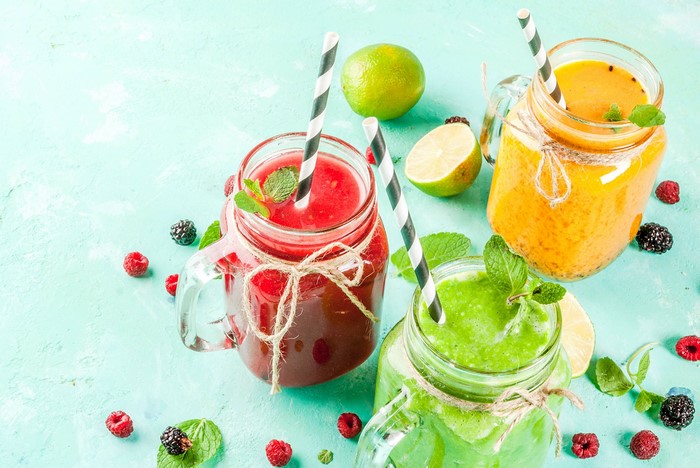 Three colorful smoothies in mason jars with berries and lime
