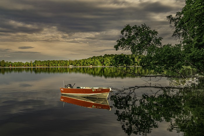 Red boat on a calm lake with trees and clouds