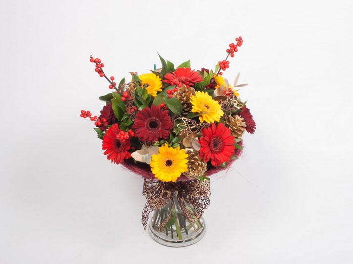 Red and yellow gerbera bouquet with pinecones and berries in a vase