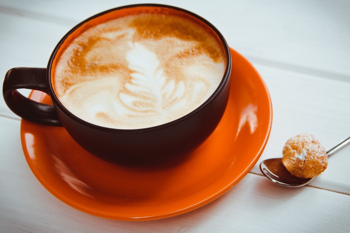 Cappuccino in a dark cup on an orange saucer with a pastry