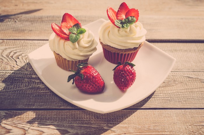Two strawberry cupcakes with cream and strawberries on a plate