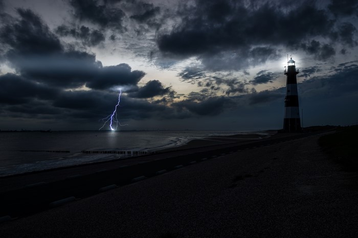 Lightning strikes near a lighthouse on the coast at night