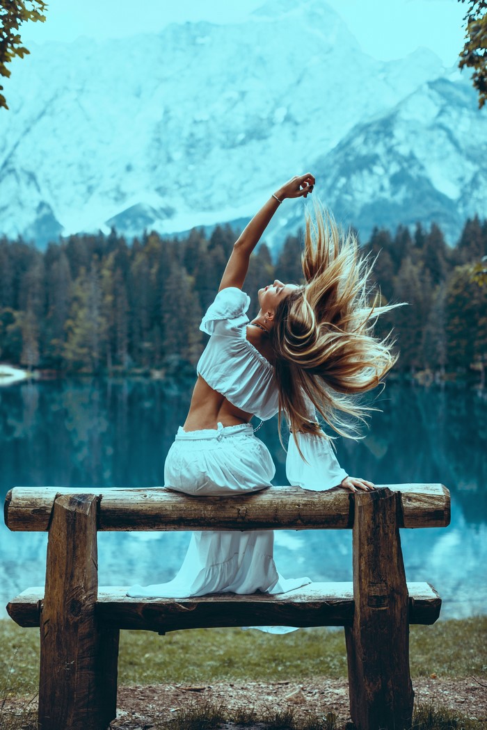Woman with blonde hair sitting on a wooden bench by a lake