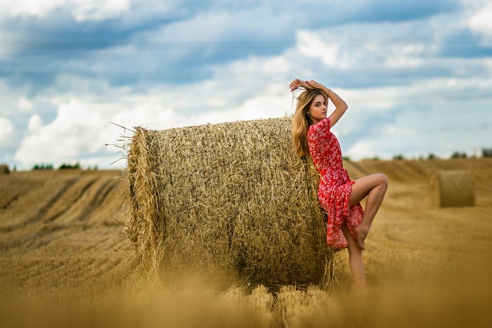 Woman in red dress posing by hay bale in field