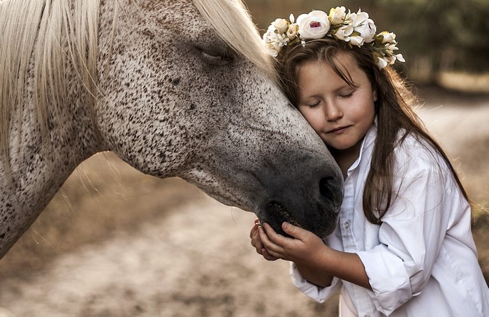 Girl with flower wreath hugging a horse