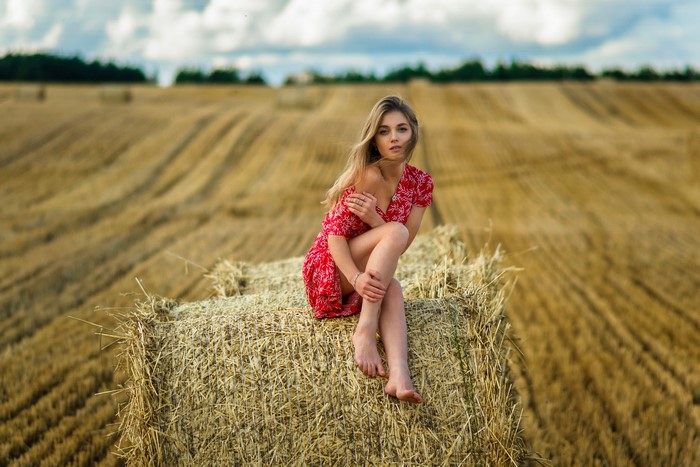 Woman in red dress sitting on hay bale in field