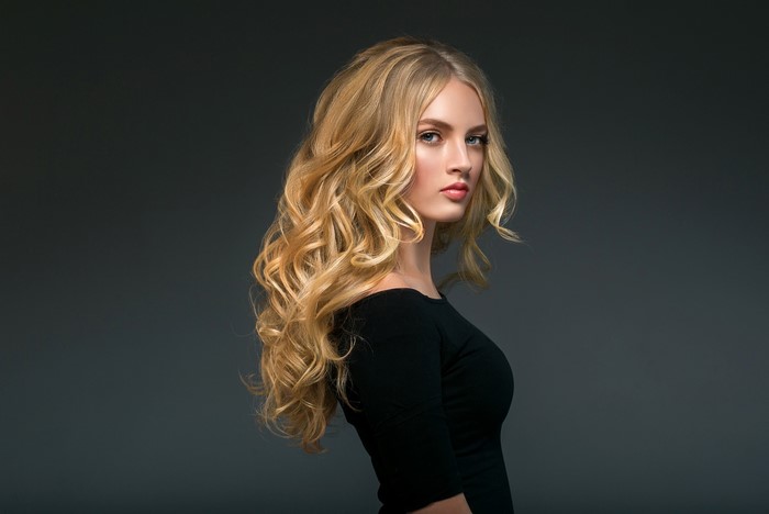 Blonde woman with curly hair on gray background