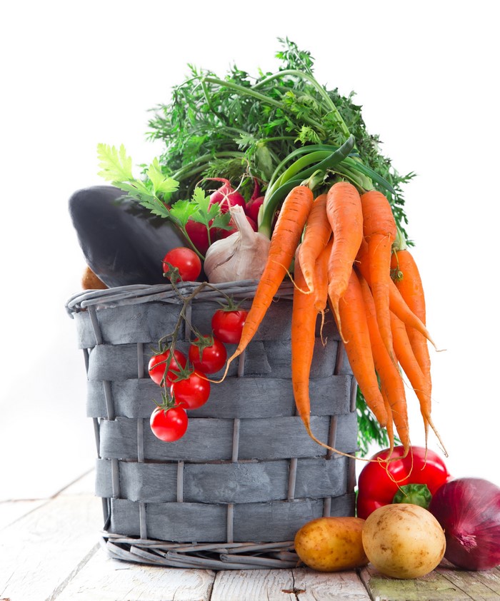 Basket of fresh vegetables including carrots, tomatoes, and eggplant