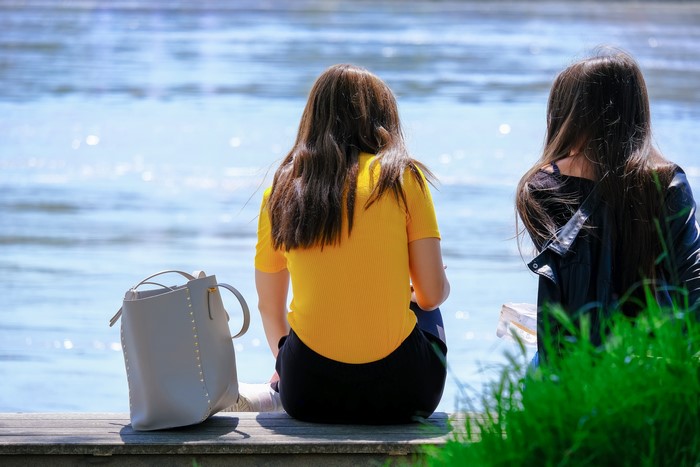 Two women sitting on a bench by the water