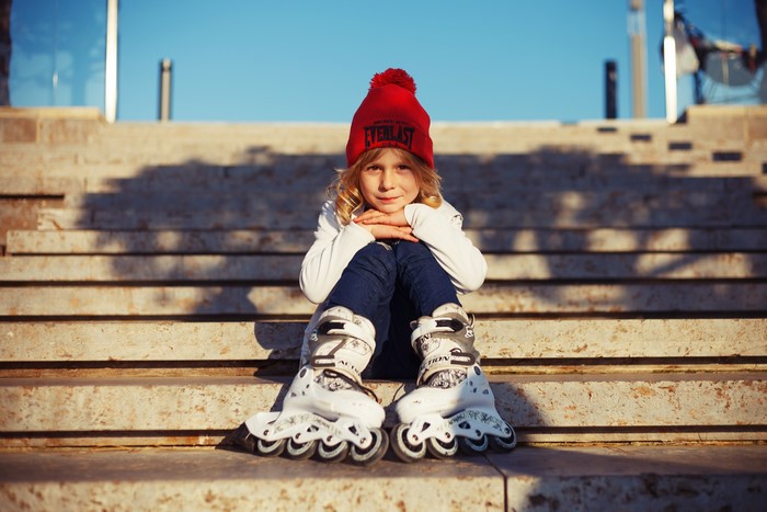 Girl in Everlast winter hat and roller skates sitting on steps