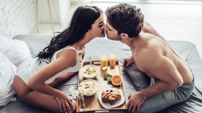 Couple kissing in bed with breakfast tray