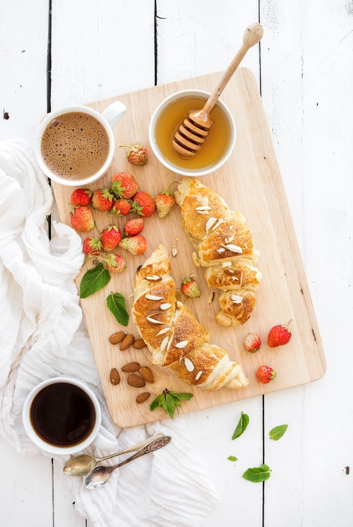Croissants with strawberries, coffee, and honey on a cutting board