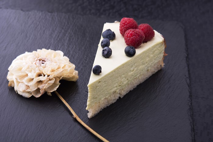 Slice of cheesecake with berries and a dried flower