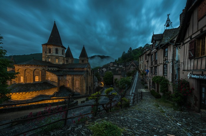 Church and medieval street in Conques, France at dusk