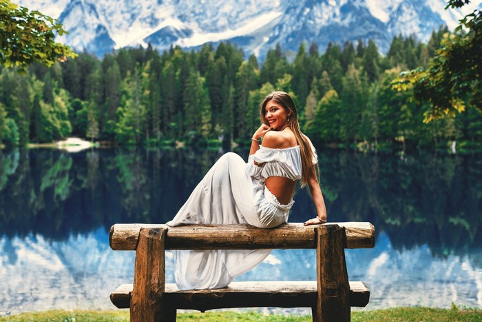 Woman in a dress sitting on a bench by a lake