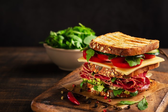 Sandwich with sausage, cheese, tomatoes, and salad