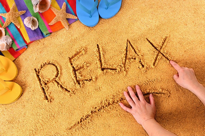 Word RELAX written in sand on a beach with flip-flops and starfish