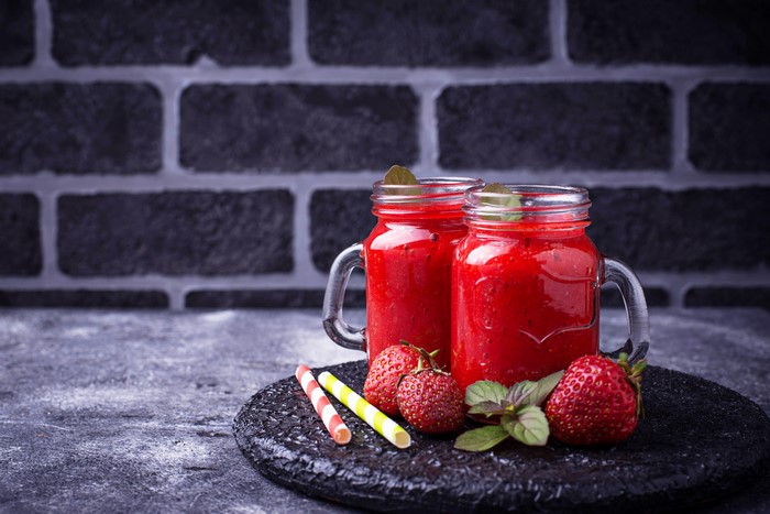 Two strawberry smoothies in mason jars with strawberries