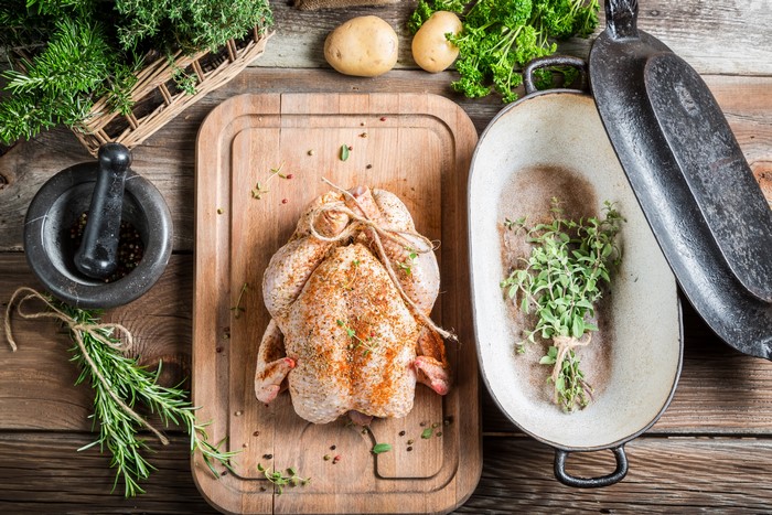 Raw chicken on cutting board with herbs and potatoes