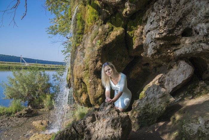 Blonde girl in dress near waterfall and rocks