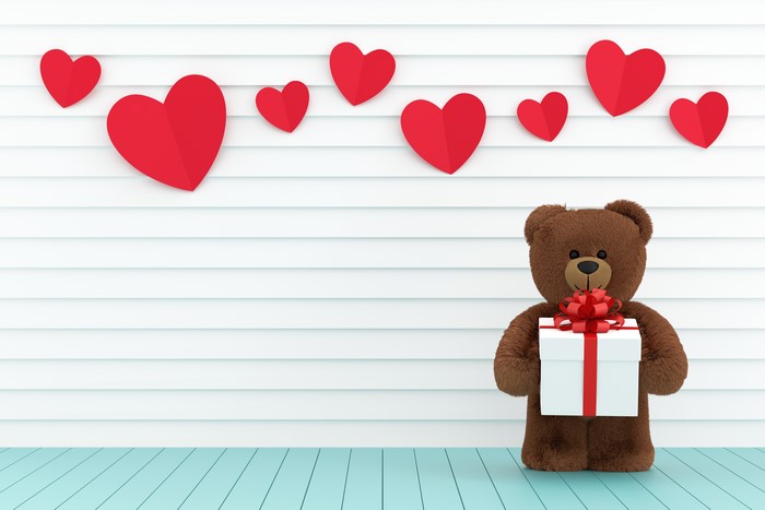 Teddy bear holding a gift with red hearts
