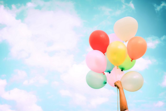 Hand holding colorful balloons against a cloudy sky
