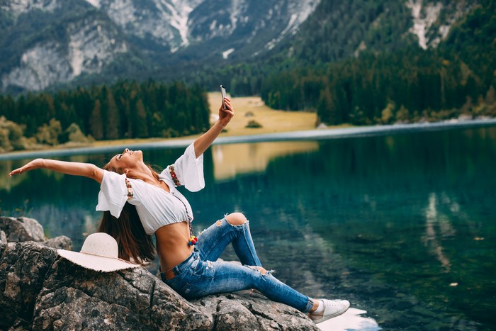Woman taking a selfie by a lake with mountains