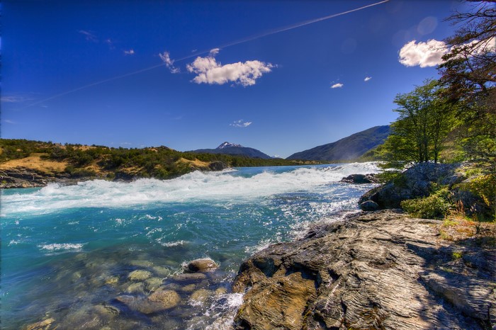 River rapids flowing past rocky shore with mountains in background