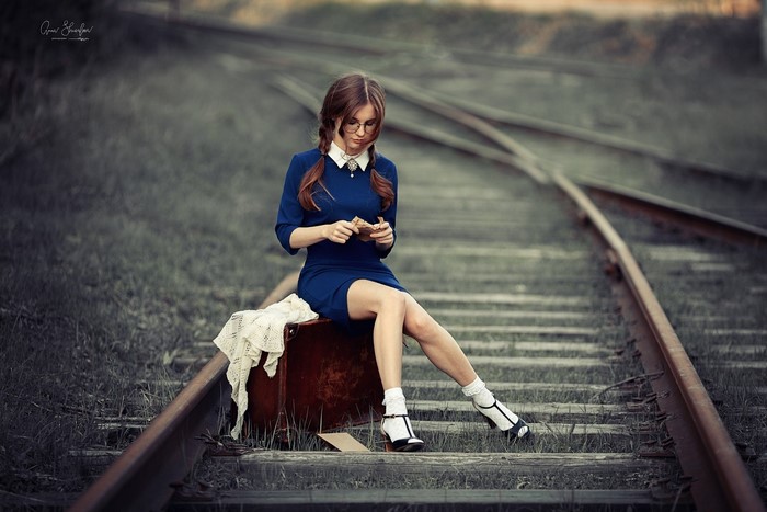 Anna Shuvalova sitting on a suitcase on railroad tracks