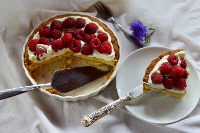 Raspberry pie with whipped cream and a slice on a plate