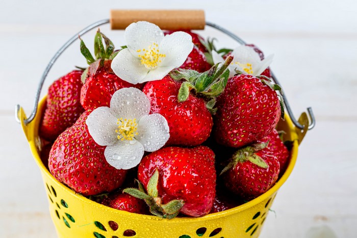 Strawberries in a yellow bucket with flowers