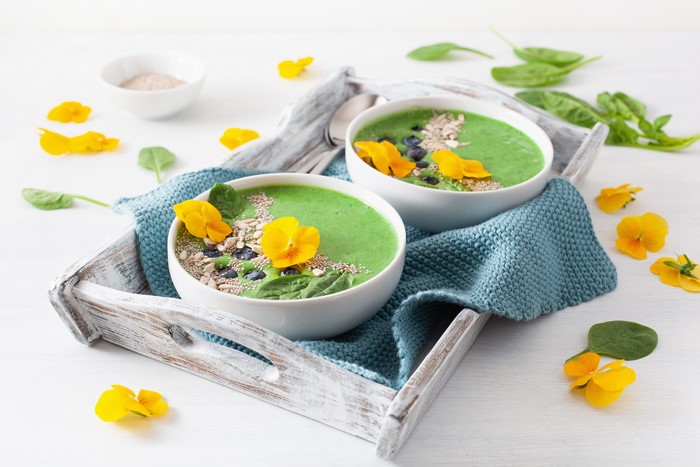 Two green smoothie bowls with flowers and seeds