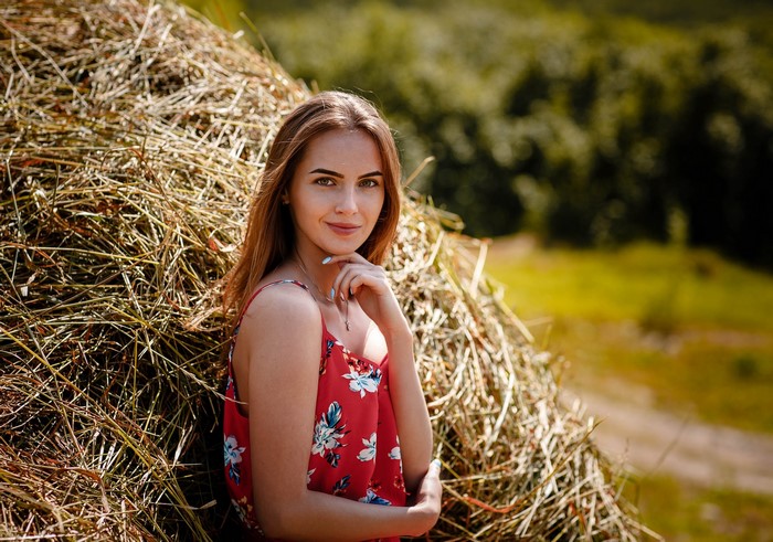 Woman in red floral dress leaning on hay bale