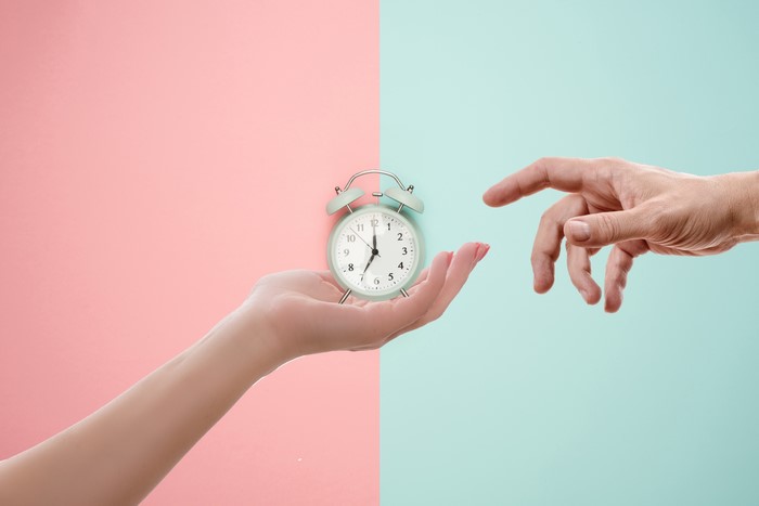 Hands and Alarm Clock on Pink and Blue Background