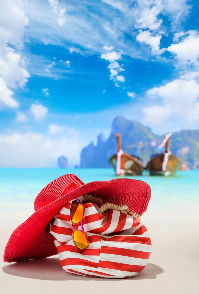 Beach scene with red hat, striped bag, and sunglasses