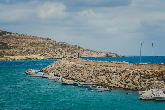 Boats docked at a rocky harbor with a lighthouse on Gozo, Malta