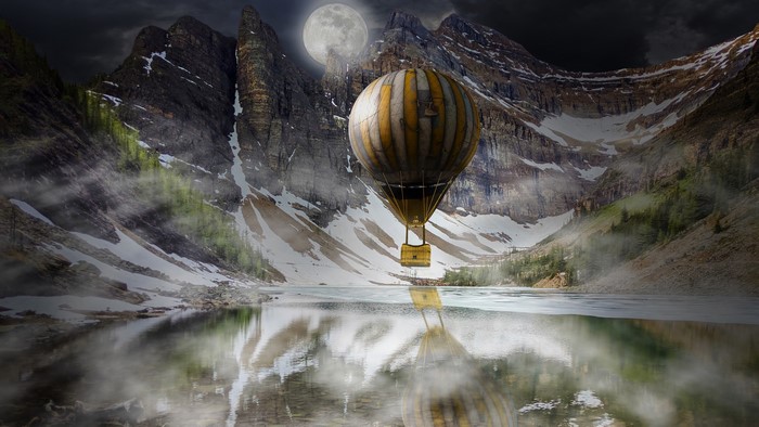 Hot air balloon over a mountain lake at night